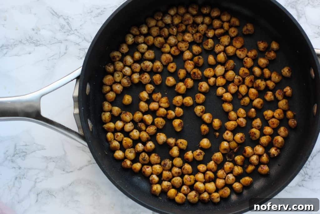 Chickpeas sizzling in a pan with olive oil and spices, achieving a crispy texture.