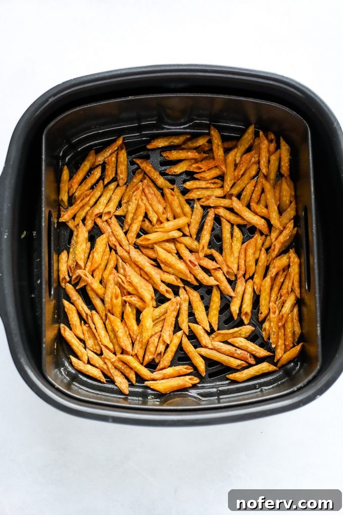 Pasta cooking in an air fryer basket, turning golden brown and crispy.