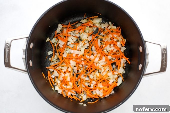 Finely chopped carrots and onions gently sautéing in a pot with olive oil, forming the aromatic base of the soup.