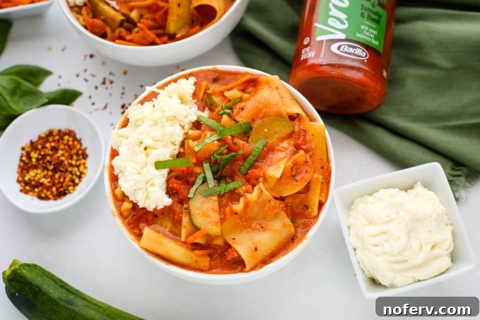 A close-up shot of vegetarian lasagna soup in a bowl, with a swirl of melted cheese and fresh basil garnish.