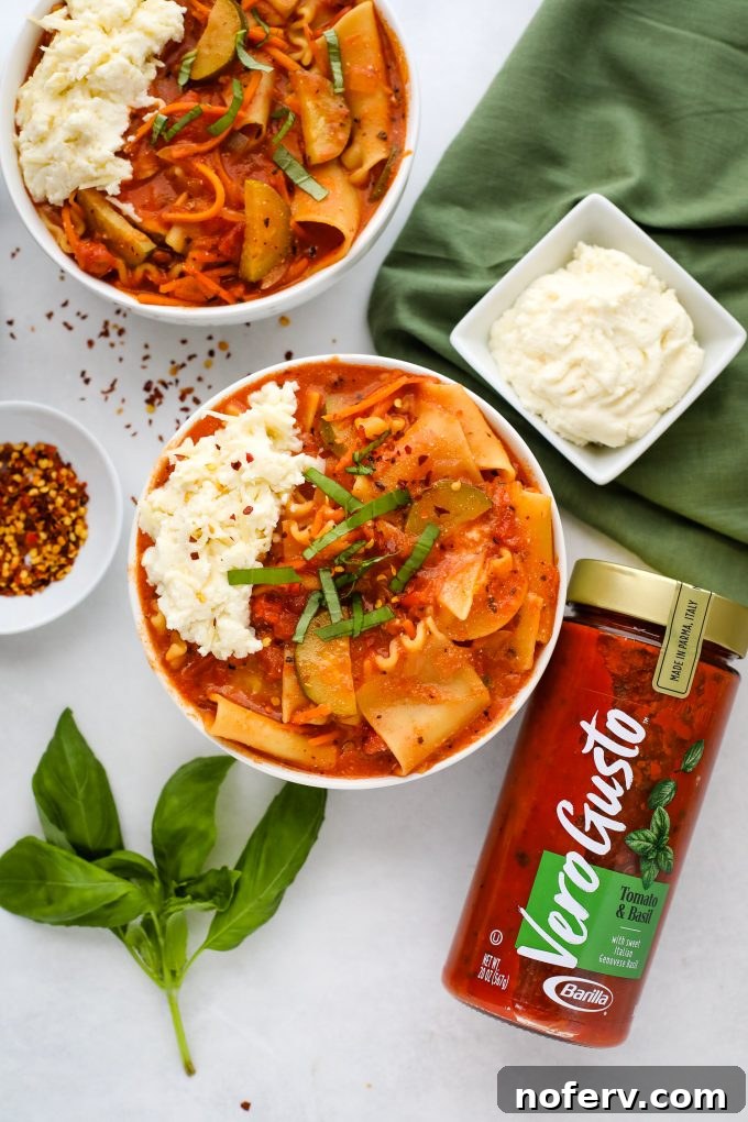 A beautifully presented bowl of vegetarian lasagna soup, garnished with fresh basil leaves and a generous dollop of creamy cheese.