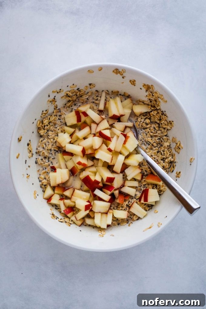 Oatmeal batter with chopped apples folded in, in a mixing bowl.