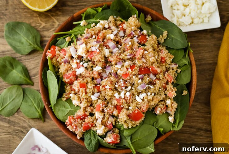 Warm Quinoa Salad served on a bed of spinach with salty feta and juicy tomatoes, a simple yet delicious side.