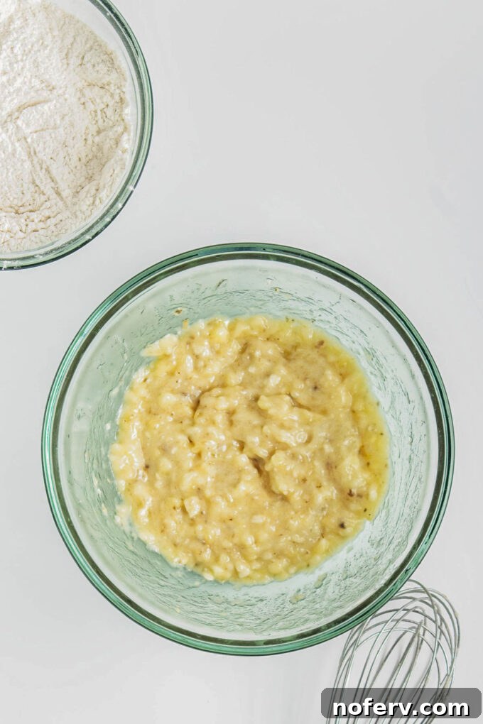 Combining mashed banana, vegetable oil, and maple syrup in a large bowl.