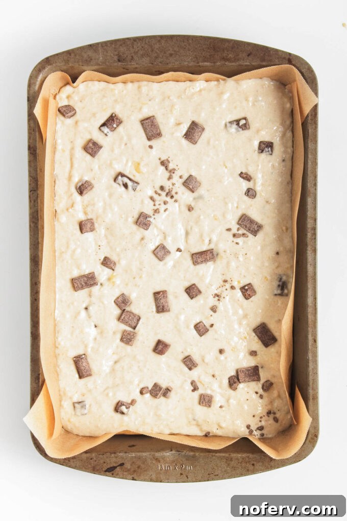 Pouring pancake batter into a prepared sheet pan and spreading it evenly.