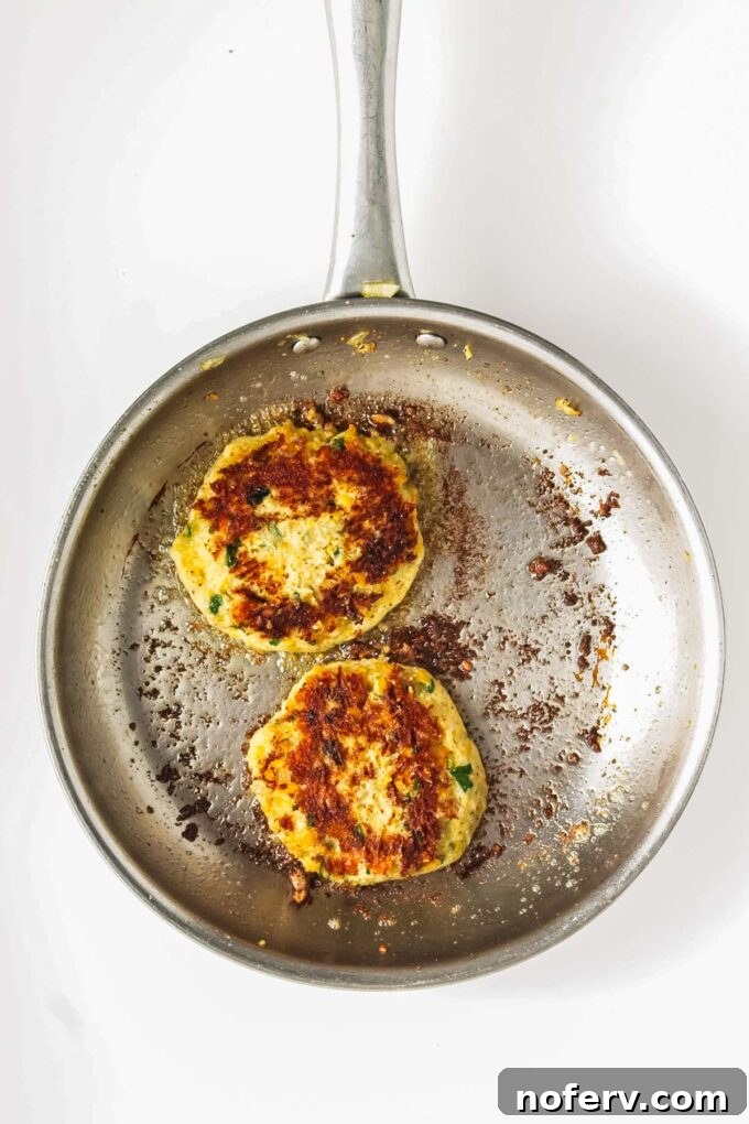 Golden Chickpea Burger Delights 9 Chickpea burgers cooking in a frying pan on the stovetop.
