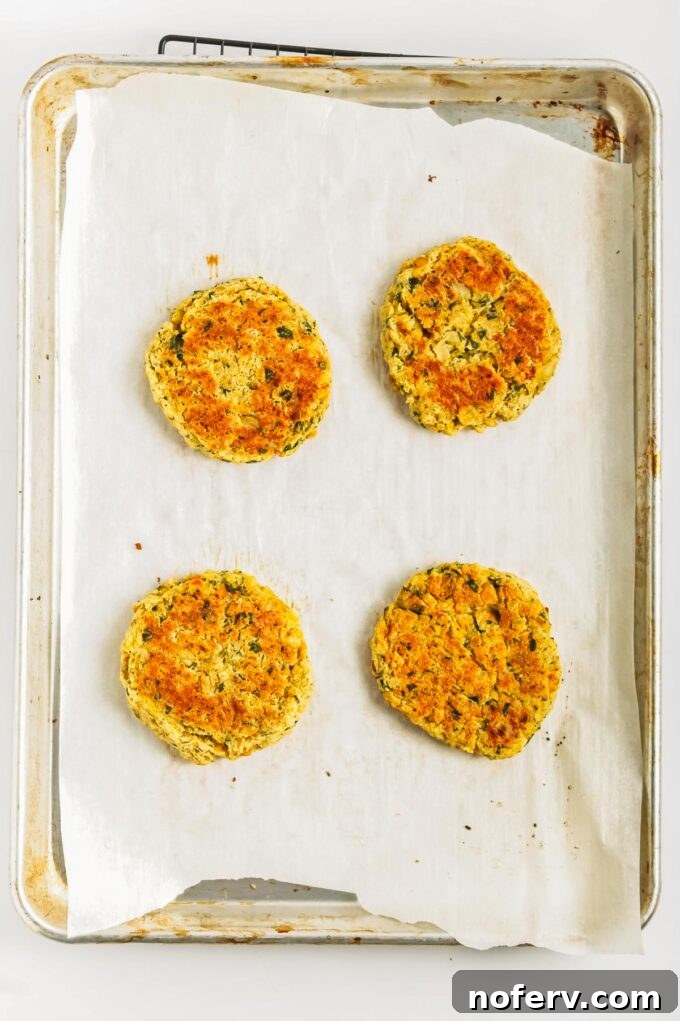 Golden Chickpea Burger Delights 10 Chickpea burgers baking on a parchment-lined tray in the oven.