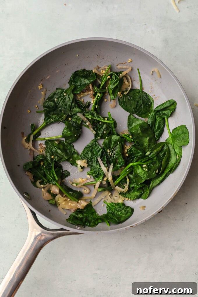 Fresh spinach wilting in a skillet with garlic and shallots