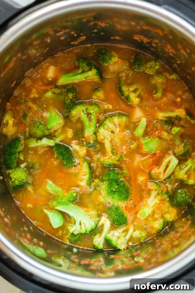 Broccoli florets and vegetable broth added to sautéed vegetables in an Instant Pot.